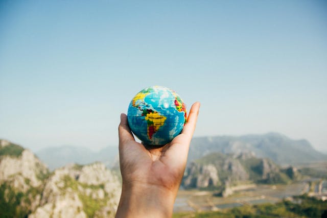 A hand holds a small globe aloft in front of a mountain range