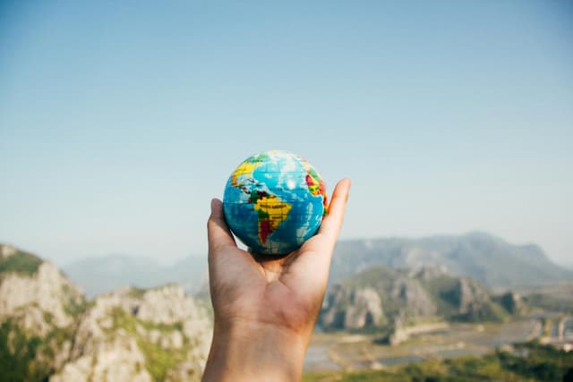 A hand holds a small globe aloft in front of a mountain range