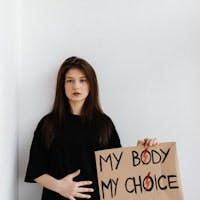 Woman with her right hand on her belly and her left hand holding a sign saying, "My body, my choice"