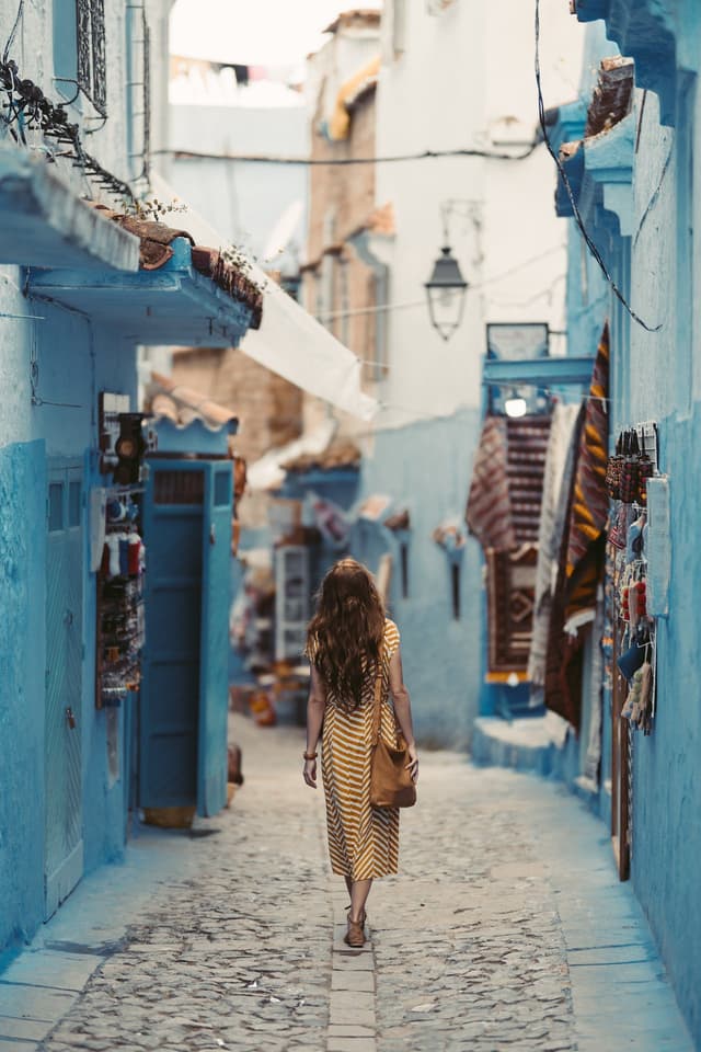 Woman walking down cobbled street with blue buildings on either side