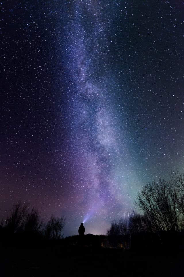 A man with a head lamp looking up into a starry sky